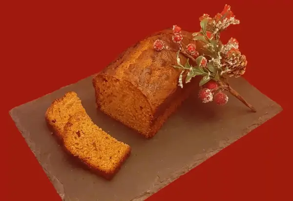 Un délicieux pain d'épice, décoré de baies rouges et de branches givrées, est prêt à être dégusté. Une tranche est déjà coupée.