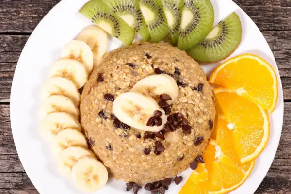 Un délicieux bowl cake flocon d'avoine, garni de rondelles de banane, de tranches de kiwi et d'orange, parsemé de pépites de chocolat.