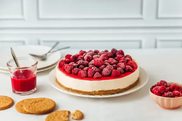 Un délicieux cheesecake framboise, garni de fruits rouges givrés, prêt à être dégusté avec un coulis et des biscuits.