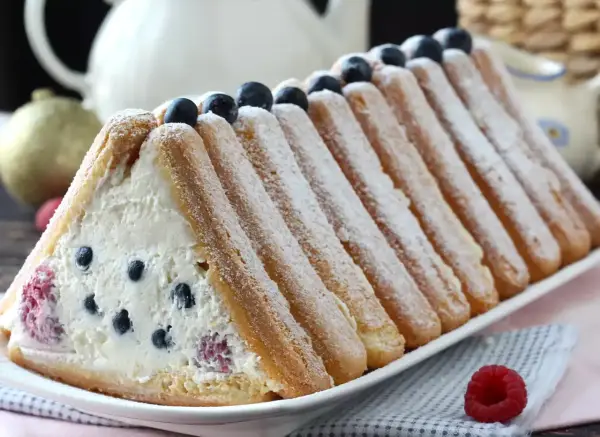 Délicieuse recette buche fruits rouges : un gâteau léger garni de crème et de baies, entouré de biscuits à la cuillère saupoudrés de sucre glace.