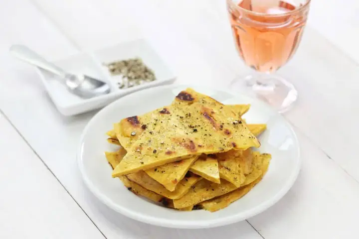 Une assiette de socca à la poêle, coupée en triangles et saupoudrée de poivre, à côté d'un verre de rosé.